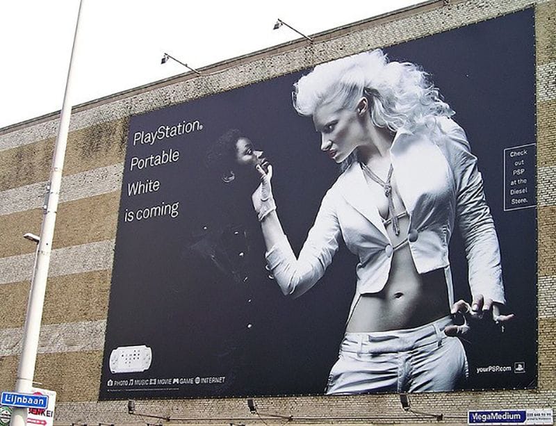 Outdoor polêmico promovendo o PlayStation Portable White (PSP branco) da Sony, com a frase "White is coming" (O branco está chegando). No anúncio, uma mulher branca, vestida completamente de branco, agarra o rosto de uma mulher negra, que está em segundo plano e vestida de preto. A mulher branca é representada de forma dominante, enquanto a mulher negra parece ser subjugada. Esse anúncio gerou muita controvérsia por seu conteúdo racista, já que visualmente insinua uma narrativa de superioridade racial, com o branco sendo exaltado de maneira agressiva sobre o negro. Embora o objetivo fosse promover o novo modelo branco do console, a composição visual e a mensagem implícita geraram críticas intensas sobre o uso de estereótipos raciais para fins comerciais.