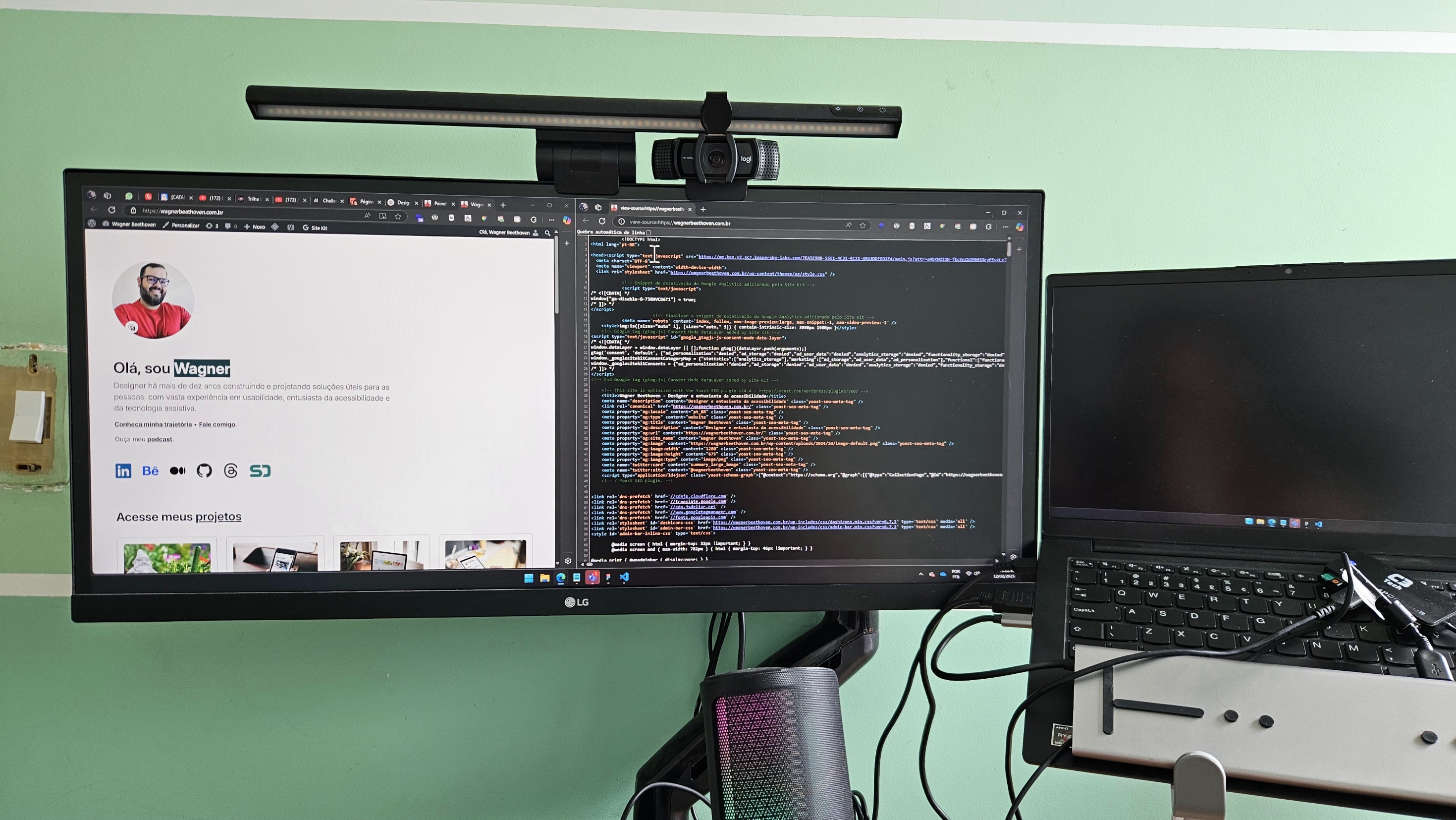 Setup de trabalho com dois monitores e um notebook. O monitor principal exibe duas abas do navegador abertas: uma mostrando o site pessoal de Wagner Beethoven, com sua foto e descrição profissional, e a outra com código-fonte. Acima do monitor há uma webcam com uma barra de luz. O segundo monitor, um notebook, está ao lado direito e tem a tela desligada. Na mesa, há um suporte para o notebook e alguns cabos conectados